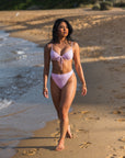 Woman walking on a beach wearing Blossom Bottom high-waisted pink bikini, showcasing its flattering cut and cheeky coverage.