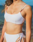 Woman wearing the Daisy Top in white, featuring push-up padding, adjustable straps, and rose gold trimming. Ideal for yoga or beach, offering comfort and support.
